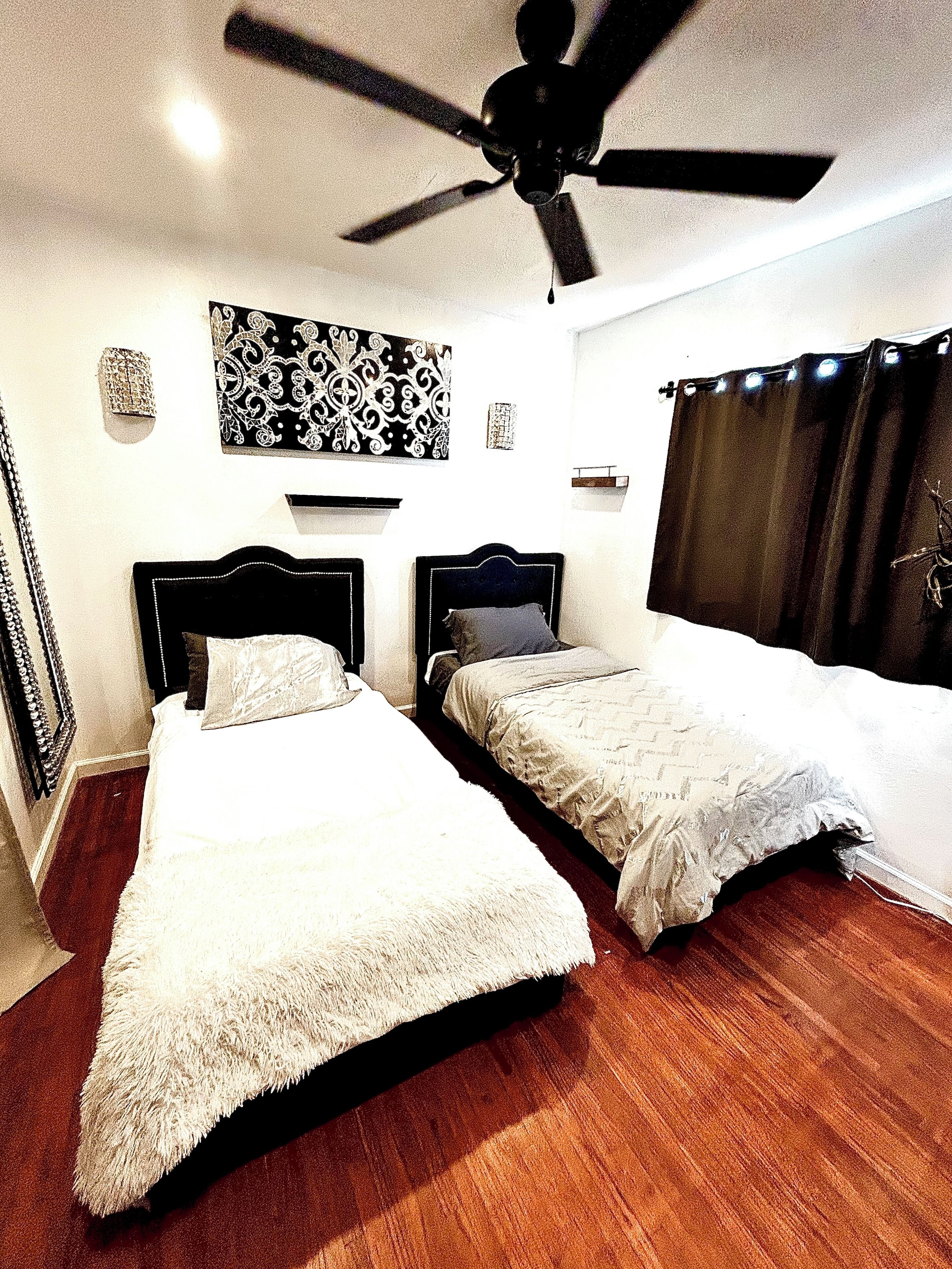 A bedroom with two beds, a ceiling fan, and a window with curtains.