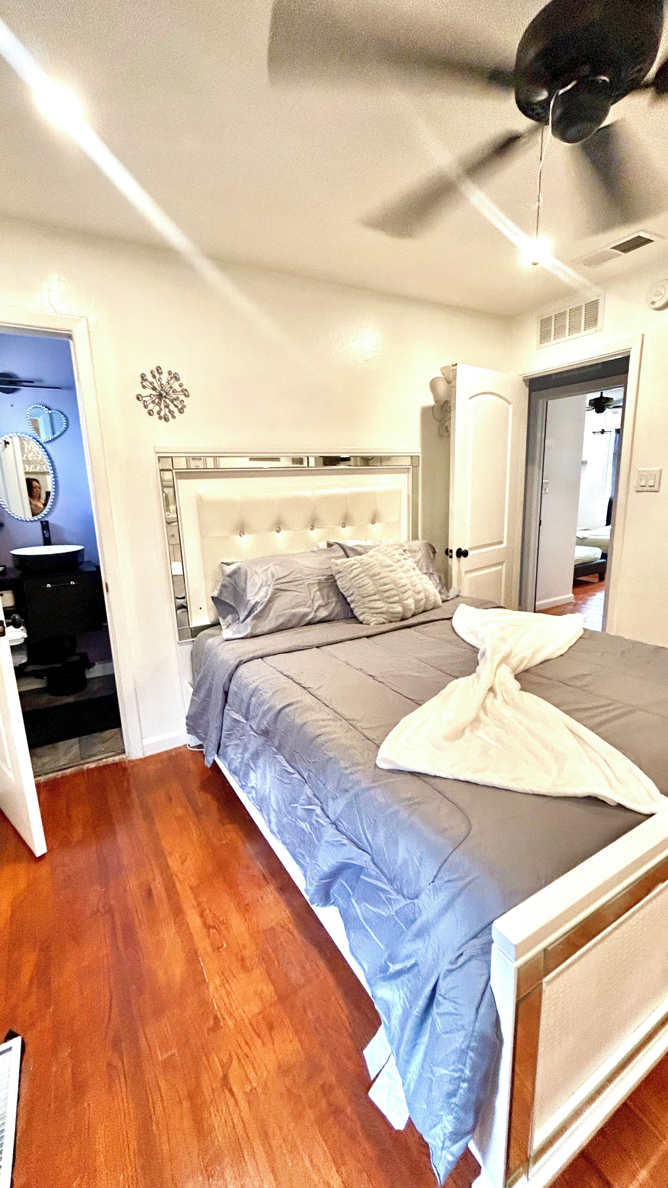 A bedroom with a bed, a ceiling fan, a bedside table, and a mirror.