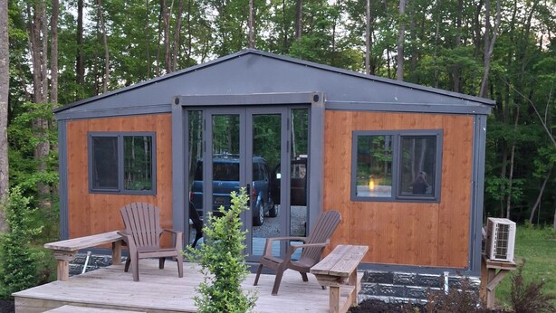A small wooden cabin with a deck, two chairs, and a bench.