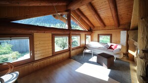 Amplia habitación en el ático con vigas de madera, ventanas grandes, un sofá blanco y una pequeña mesa.