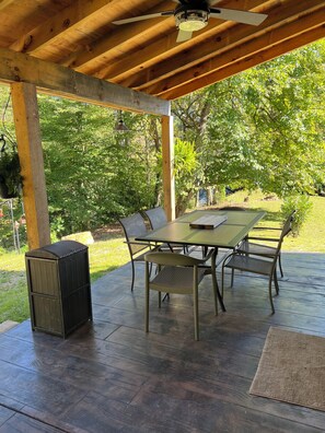 An outdoor patio with a wooden table and chairs, a ceiling fan, and a trash can. - Willow Cabin- Private 2 BR Cabin (Johnson City)