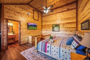 A wooden cabin interior with a bed, a ceiling fan, and a television. - 6-Bedroom Cabin with Indoor Pool, Movie Theater & Hot Tub Near Dollywood (Sevierville)