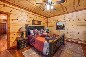 Ein Schlafzimmer in einer Holzhütte mit einem Bett, Nachttischen, einer Lampe und einem Deckenventilator.