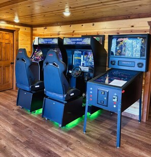 A gaming area with three racing game stations and a central console. - 6-Bedroom Cabin with Indoor Pool, Movie Theater & Hot Tub Near Dollywood (Sevierville)