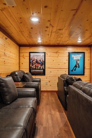 A room with wooden walls and ceiling, featuring two black leather sofas and two posters on the wall. - 6-Bedroom Cabin with Indoor Pool, Movie Theater & Hot Tub Near Dollywood (Sevierville)