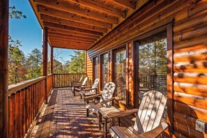 A wooden deck with Adirondack chairs and a covered area, overlooking a forested landscape. - 6-Bedroom Cabin with Indoor Pool, Movie Theater & Hot Tub Near Dollywood (Sevierville)