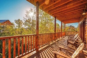 Eine Holzterrasse mit Geländer, Sitzgelegenheiten im Freien und Blick auf Bäume und Gebäude.