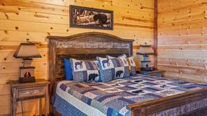 A wooden cabin room with a bed, two nightstands, and a framed picture on the wall.