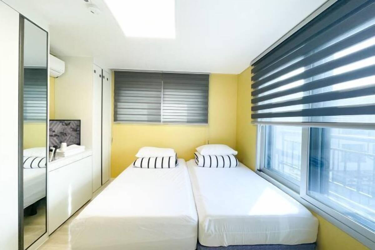 Una habitación con dos camas, un espejo, una ventana con persianas y un armario.