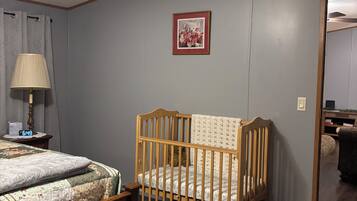 A bedroom with a wooden crib, a bed with a floral bedspread, a nightstand with a lamp, and a ceiling fan.