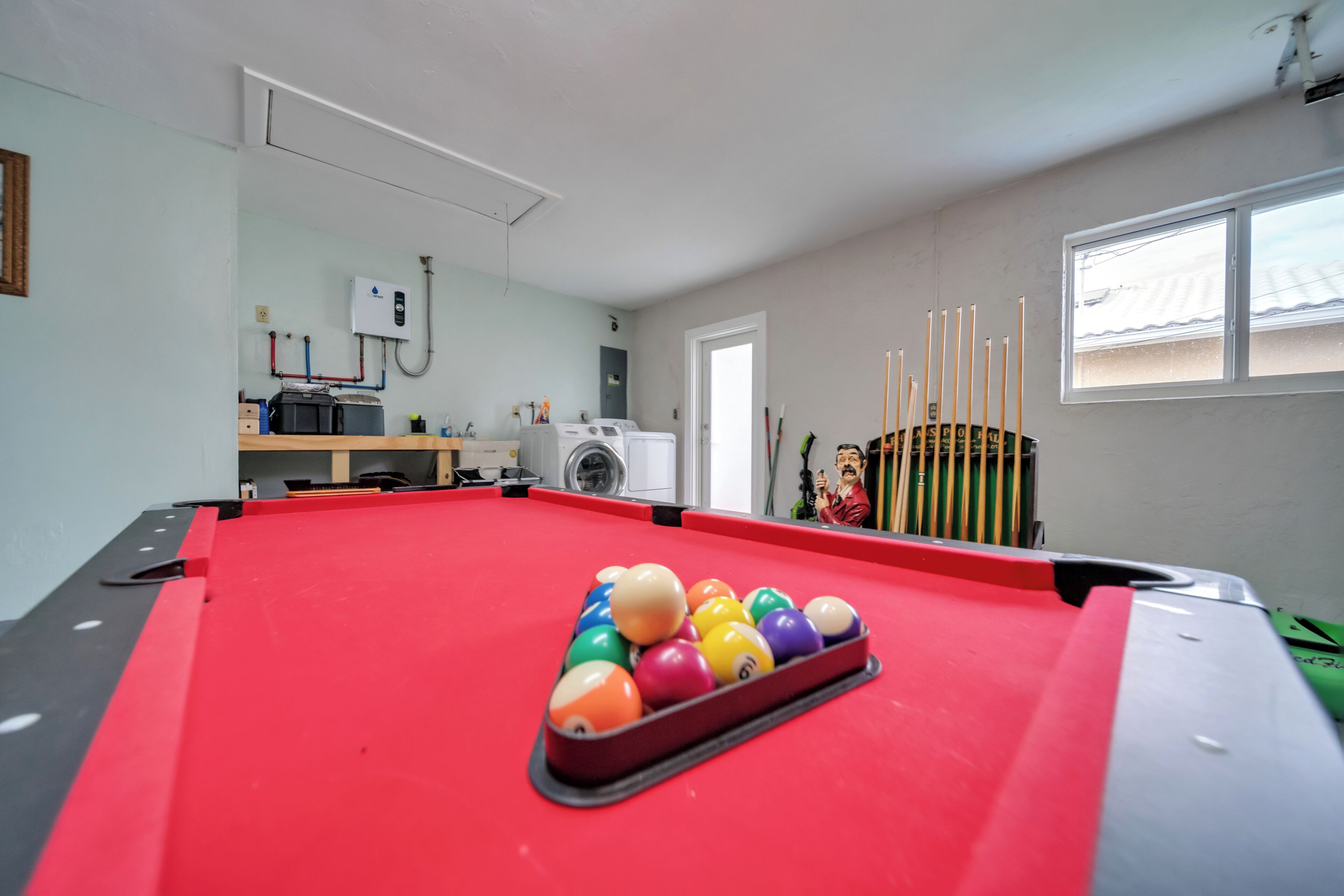 A pool table with balls, a washing machine, and a window with blinds.