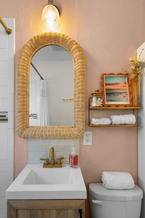 Een badkamer met een wit wastafel, een gouden kraan en een grote geweven spiegel.