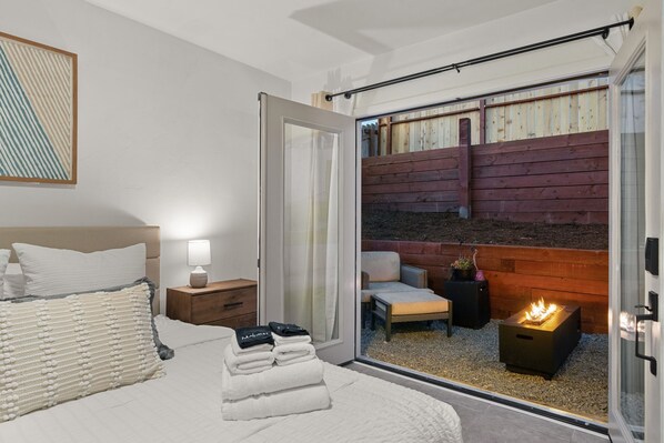 Un dormitorio con cama, mesita de noche y vistas a una terraza de madera y una chimenea.