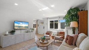 A modern living room with a flat-screen TV, a sofa, a coffee table, and a large window.