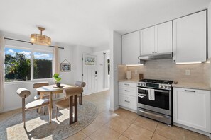 Een moderne keuken met witte kasten, een roestvrijstalen fornuis en een eethoek met een tafel en stoelen.