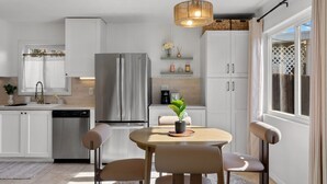 A modern kitchen with white cabinets, a stainless steel refrigerator, and a dining area with a round table and chairs.