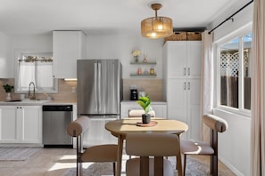 Una cocina moderna con armarios blancos, un refrigerador de acero inoxidable y un comedor con una mesa redonda y sillas.