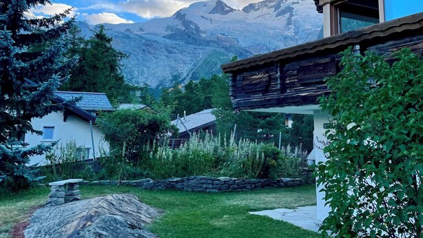 Une maison moderne avec un chemin de pierre menant à une zone herbeuse, entourée d’arbres et offrant une vue sur la montagne.