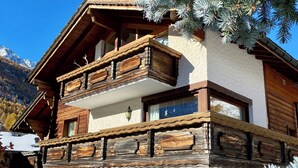 Un bâtiment de style chalet, avec une façade en bois, des murs extérieurs blancs et un balcon doté de balustrades en bois.
