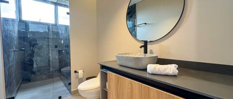 A modern bathroom with a glass shower enclosure, a round mirror, and a wooden vanity.