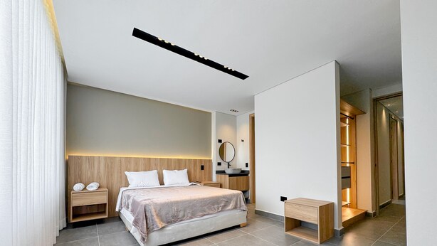 Un dormitorio moderno con una cama grande, mesitas de noche, un espejo junto a la cama y un pequeño banco de madera.
