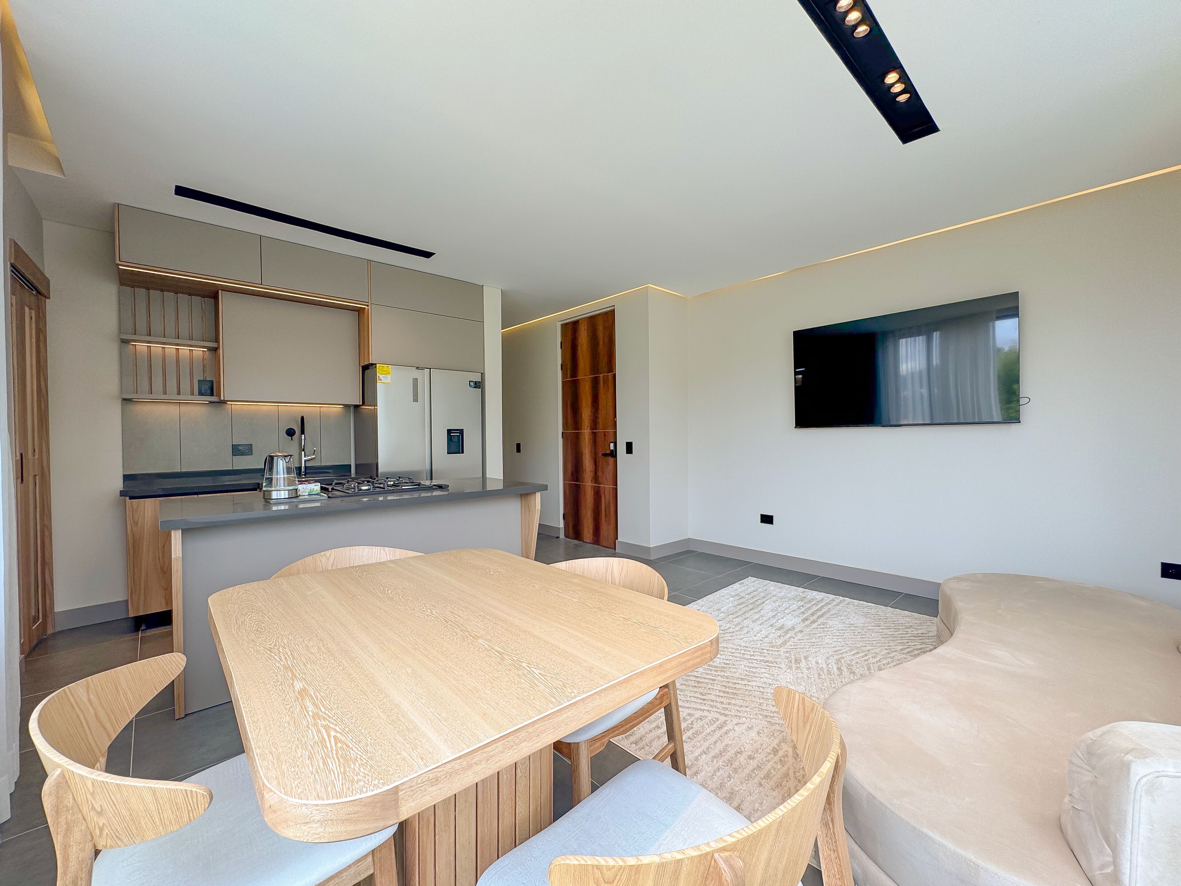 Een moderne keuken met een centraal eiland, houten stoelen, een beige bank en een flatscreen televisie aan de wand.