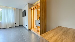Una habitación de hotel moderna con un mostrador de recepción de madera, un televisor de pantalla plana montado en la pared y un ventanal con cortinas de gasa.