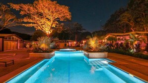 A swimming pool with a night view, surrounded by well-lit trees and a building with a poolside area. - Surfer`s Oasis Pool Villa The Point Playa Avellana (Playa Avellanas)