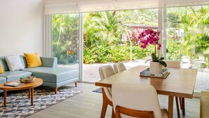 A modern living room with a sofa, coffee table, and dining table, large windows with a view of tropical plants. - Surfer`s Oasis Pool Villa The Point Playa Avellana (Playa Avellanas)