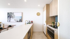 Una cocina moderna con una isla central, armarios de madera, un reloj en la pared y un cuadro con temática de playa.