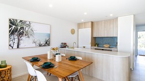 Una cocina moderna con una mesa de comedor de madera, sillas blancas y vistas al mar a través del ventanal.