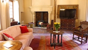A living room with a sofa, armchair, round table, fireplace, television, and a decorative vase. - Holiday Home 'L'ancien Collège' with Private Pool, Wi-Fi and Air Conditioning (Hérisson)