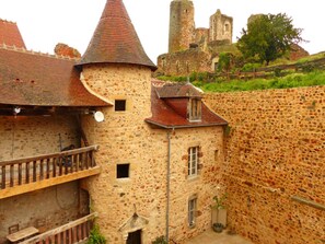 Un bâtiment en pierre doté d’une tourelle, d’un balcon et offrant une vue sur un château en arrière-plan.