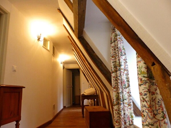 Un couloir étroit avec des poutres en bois, un banc en bois et une porte au fond.