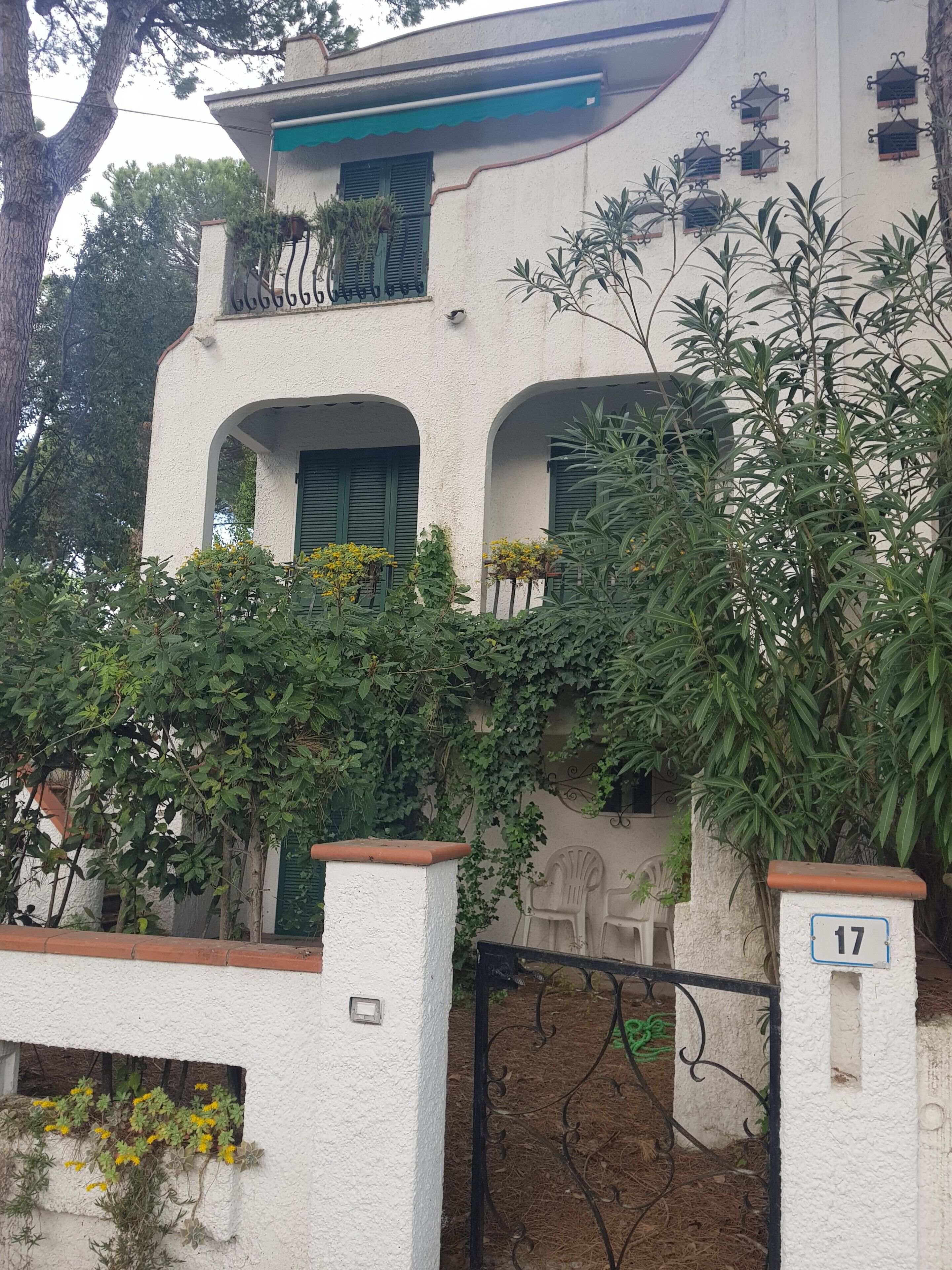 A building with a white exterior, green shutters, and a balcony with hanging plants.