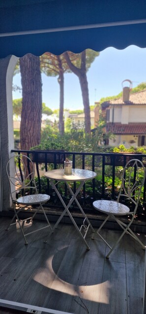 Un balcon avec deux chaises en métal et une petite table, donnant sur un jardin et des immeubles.