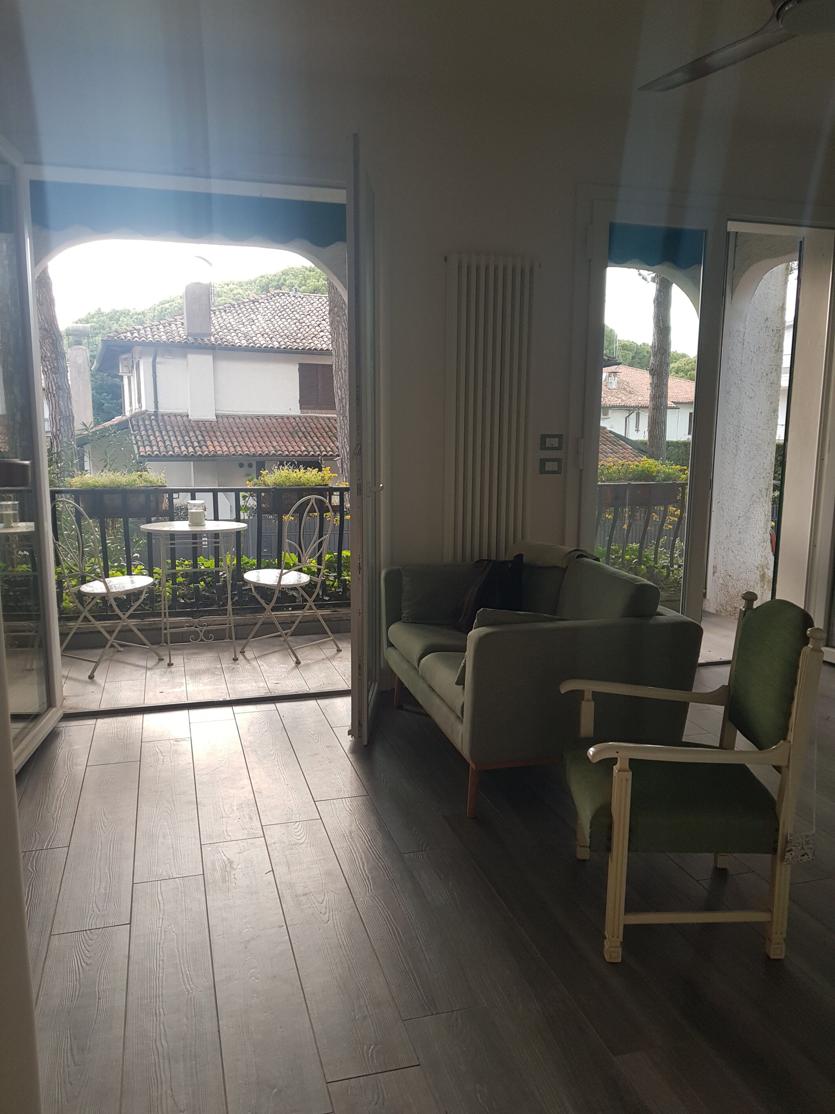 Une pièce avec un plancher en bois, un canapé vert, un fauteuil blanc et une petite table avec des chaises.