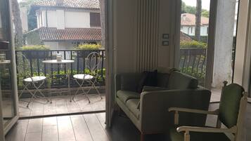 Une pièce avec un plancher en bois, un canapé vert, un fauteuil blanc et une petite table avec des chaises.