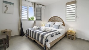Une chambre à coucher avec un lit, des tables de chevet, une fenêtre avec des volets et une vue sur la verdure.