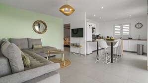 Un salon moderne avec un canapé gris, une petite table en bois et un téléviseur fixé au mur.