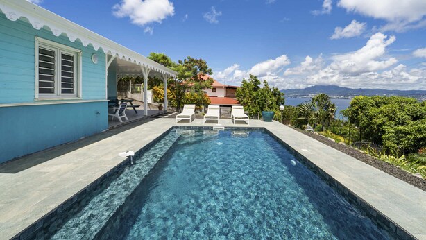 Une piscine avec des chaises longues, un patio couvert et une vue sur la mer et les montagnes.