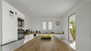 Une cuisine moderne avec des meubles blancs, une table à manger en bois et une horloge au mur.