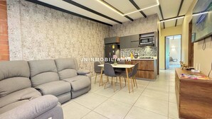 A modern living room with a grey sofa, a dining area with a table and chairs, and a kitchen with a microwave and stove. - Cabañas Cielo Verde (Rionegro)