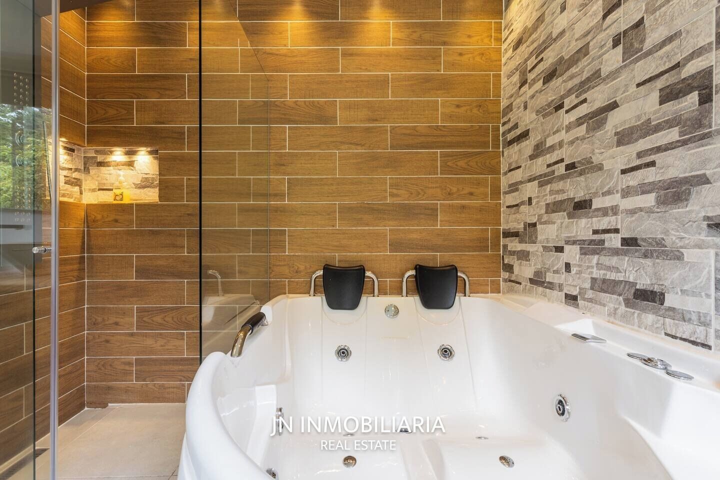 Een badkamer met een groot, wit bad, houten en stenen wandtegels en een glazen douchecabine.