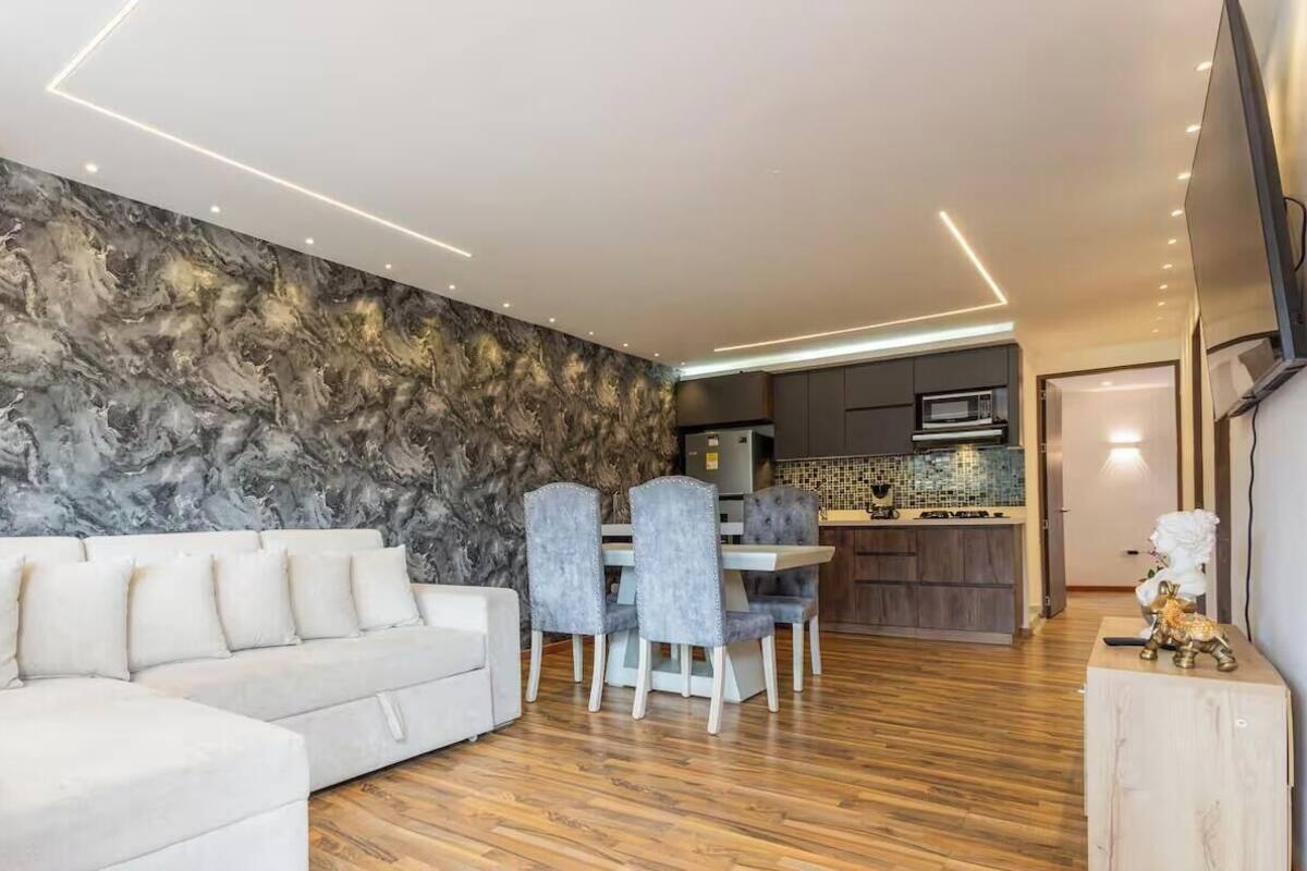 Uma sala de estar moderna com um sofá seccional, área de jantar com cadeiras e uma cozinha ao fundo.
