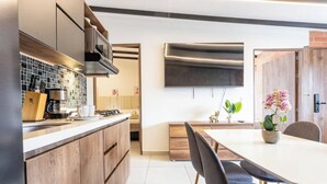 A modern kitchen with a built-in stove, microwave, and coffee maker. There is a dining area with a table and chairs, and a TV mounted on the wall. - Cabañas Cielo Verde (Rionegro)