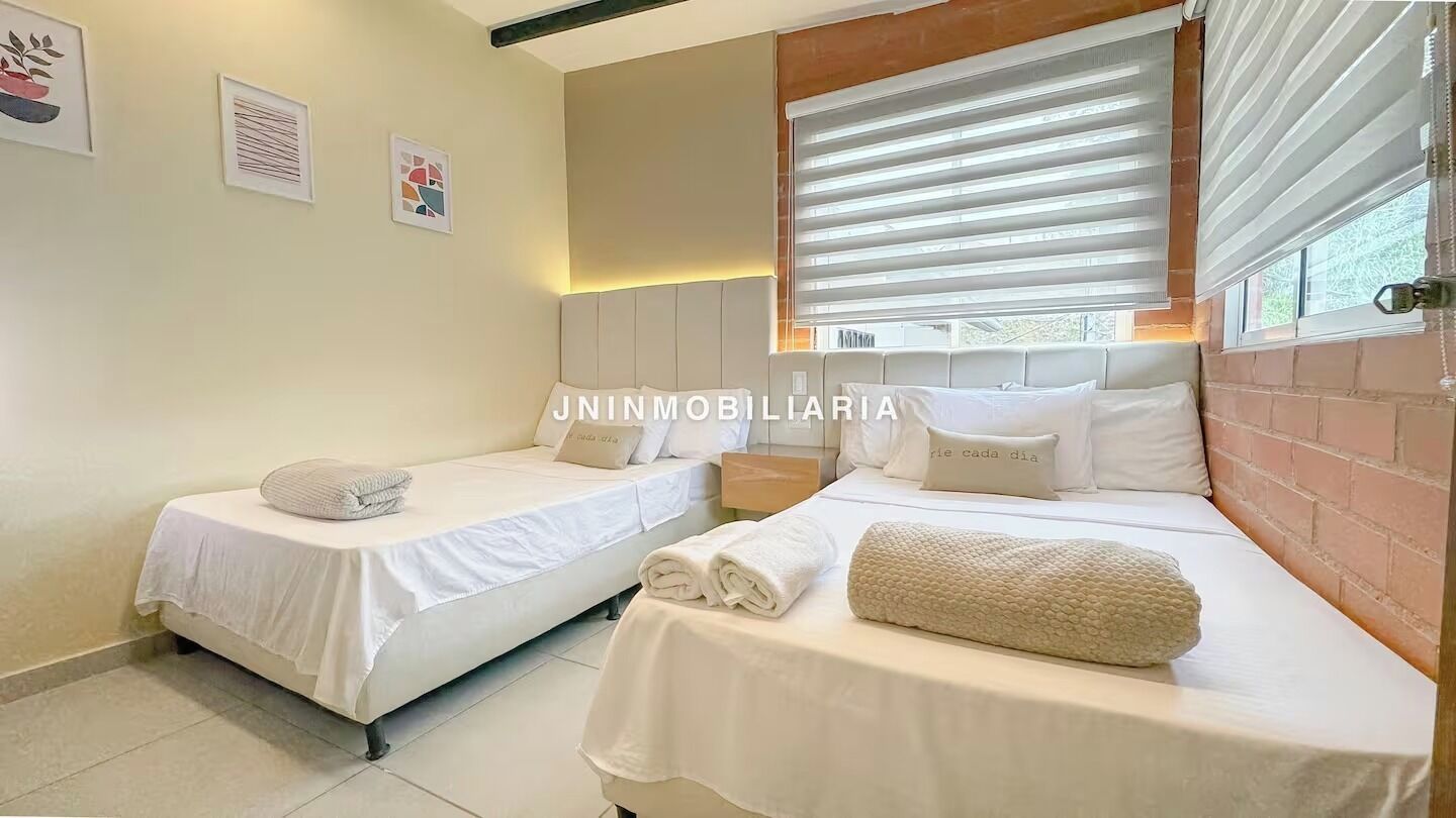 Un dormitorio con dos camas, cada una con colcha y almohadas blancas, y una ventana con persianas.