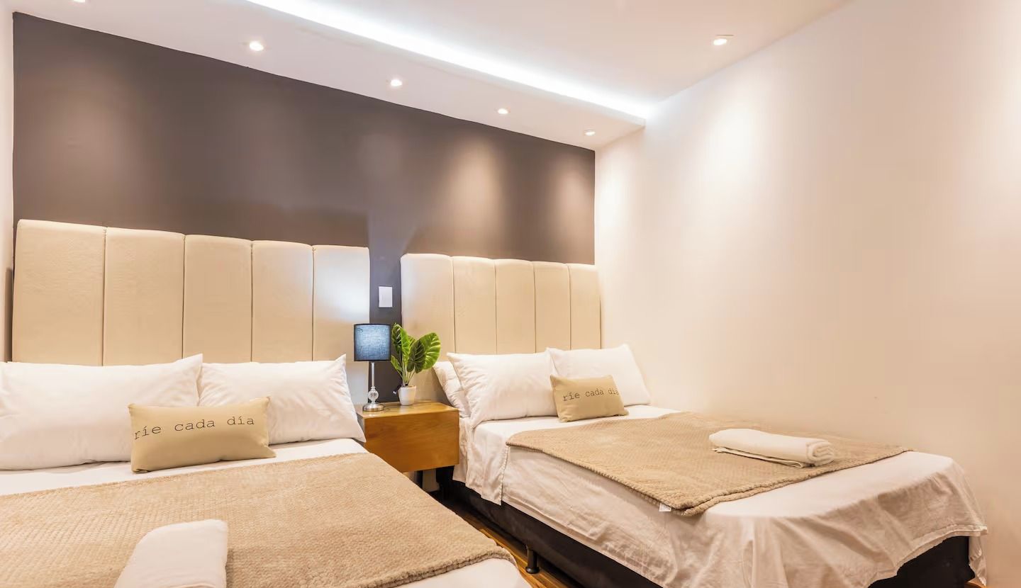 A hotel room with two beds, a bedside table with a lamp, and a plant.