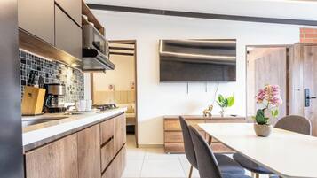 A modern kitchen with a built-in stove, microwave, and coffee maker. There is a dining area with a table and chairs, and a TV mounted on the wall.