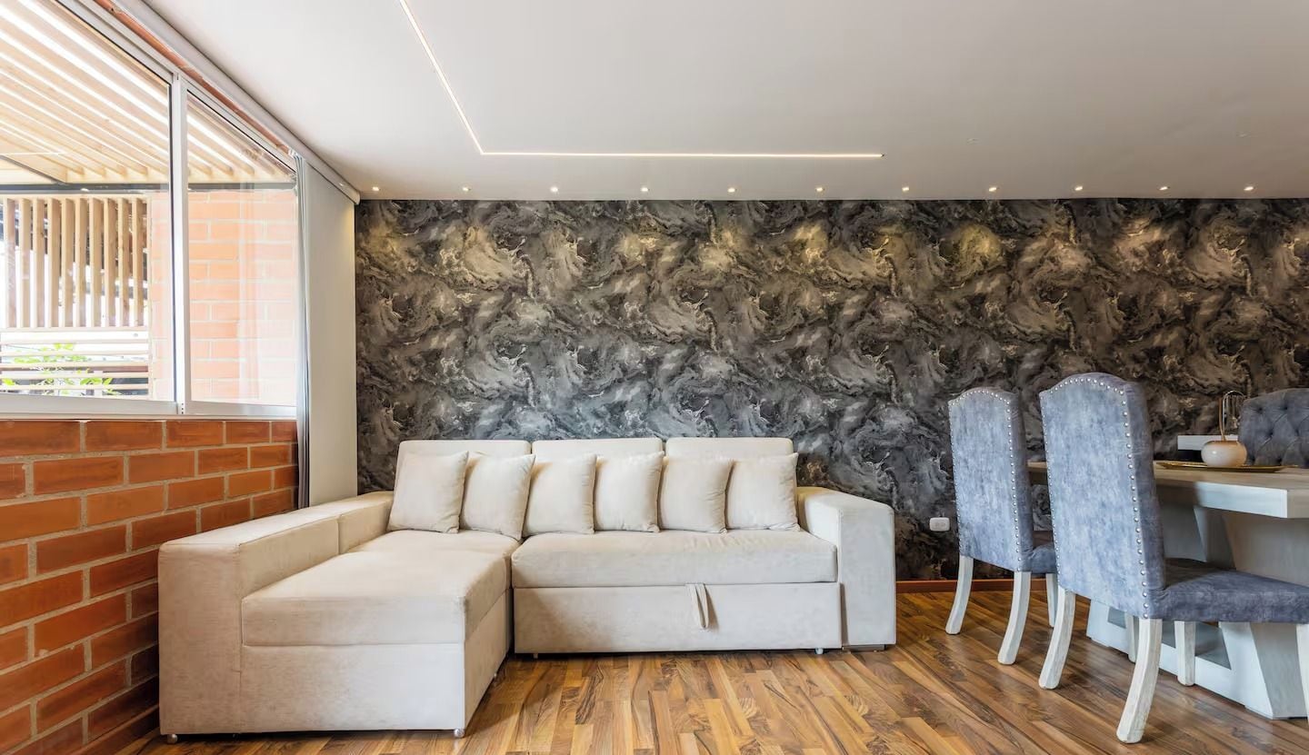 Ein modernes Wohnzimmer mit einer Eckcouch, einem Essbereich mit Stühlen und einer Ziegelwand.